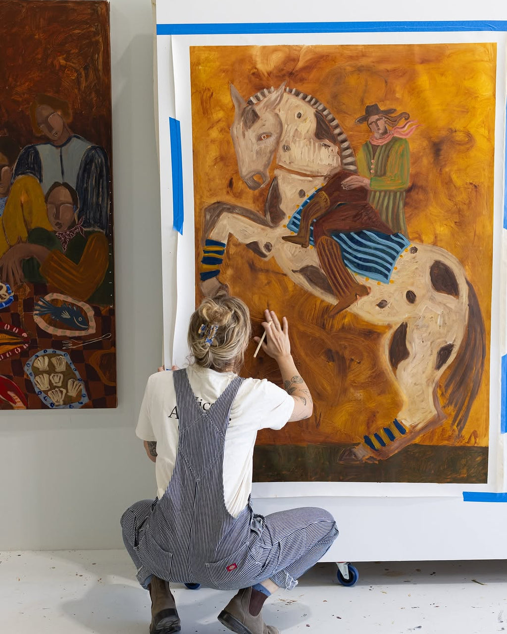 Kate florence painting a large canvas artwork of a man riding a horse. The oil painting uses warm, earthy tones that create an entrancing feel. 