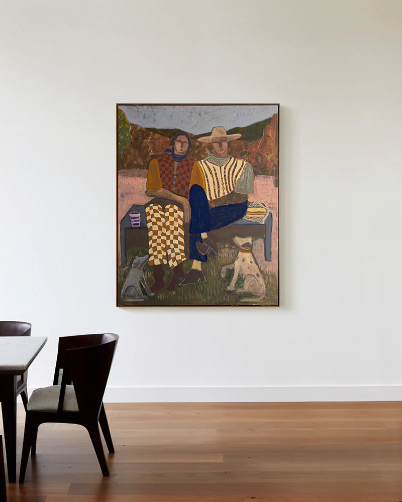 Framed painting of two people sitting on a bench with a dog, hanging on a white wall above a dining table.