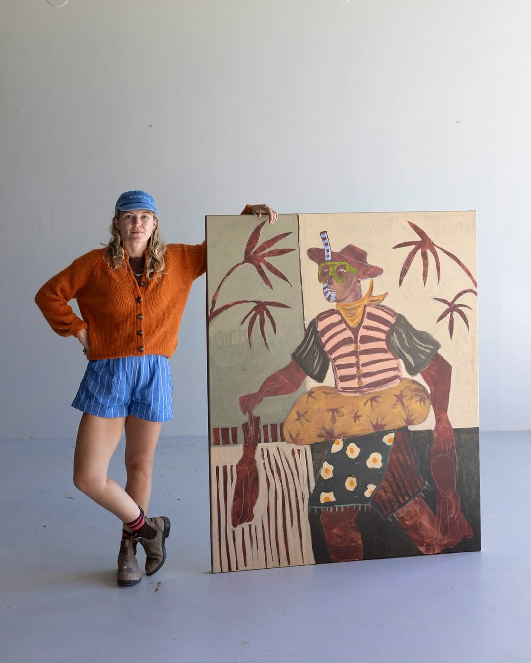 Kate Florence holding an original painting of a person in a colorful outfit against a plain background